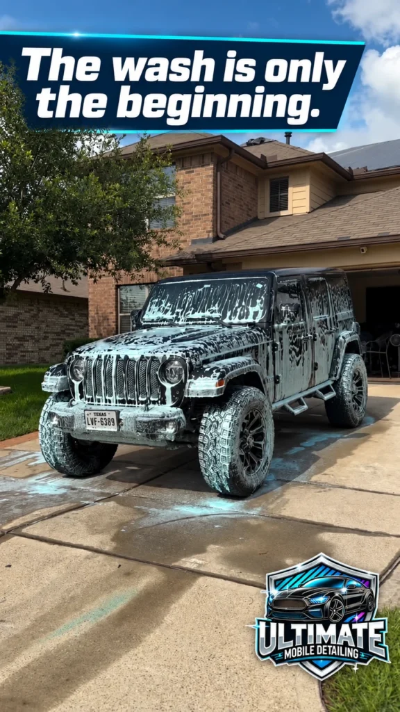 Black Jeep Wrangler covered in wash foam on a driveway beneath The wash is only the beginning banner