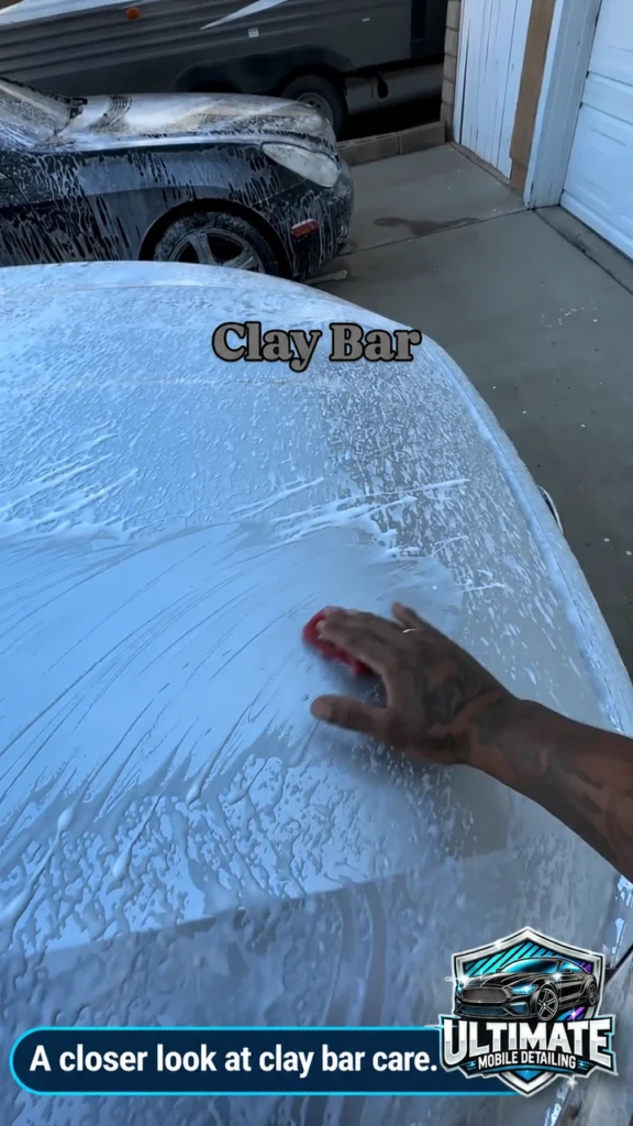 Close view of a hand guiding a red claying tool over a wet light-colored hood