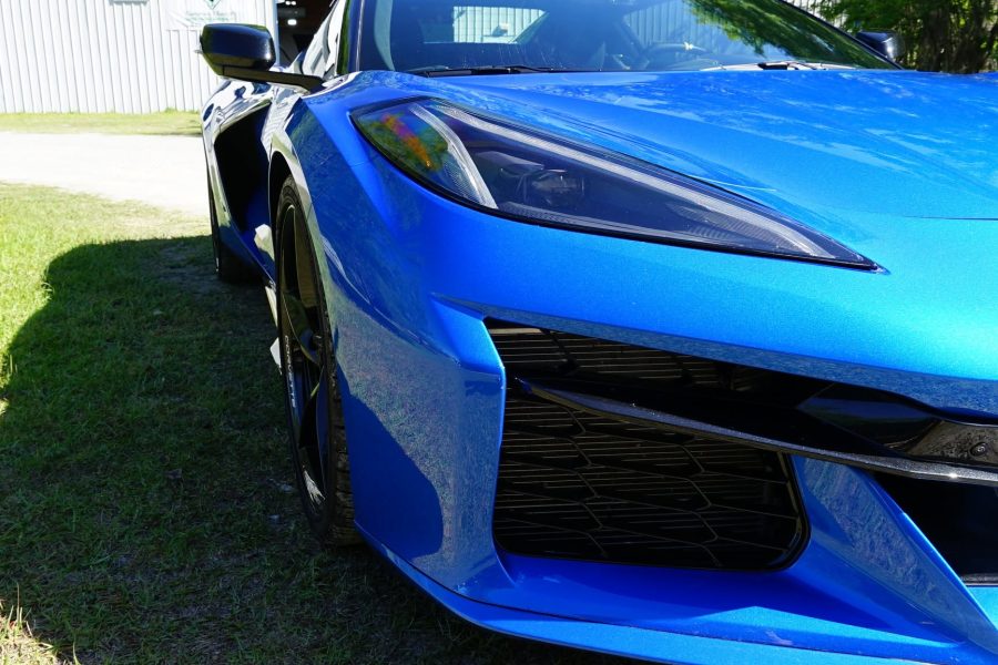 Close view of a blue sports car with reflective front bodywork, a headlamp and sculpted bumper